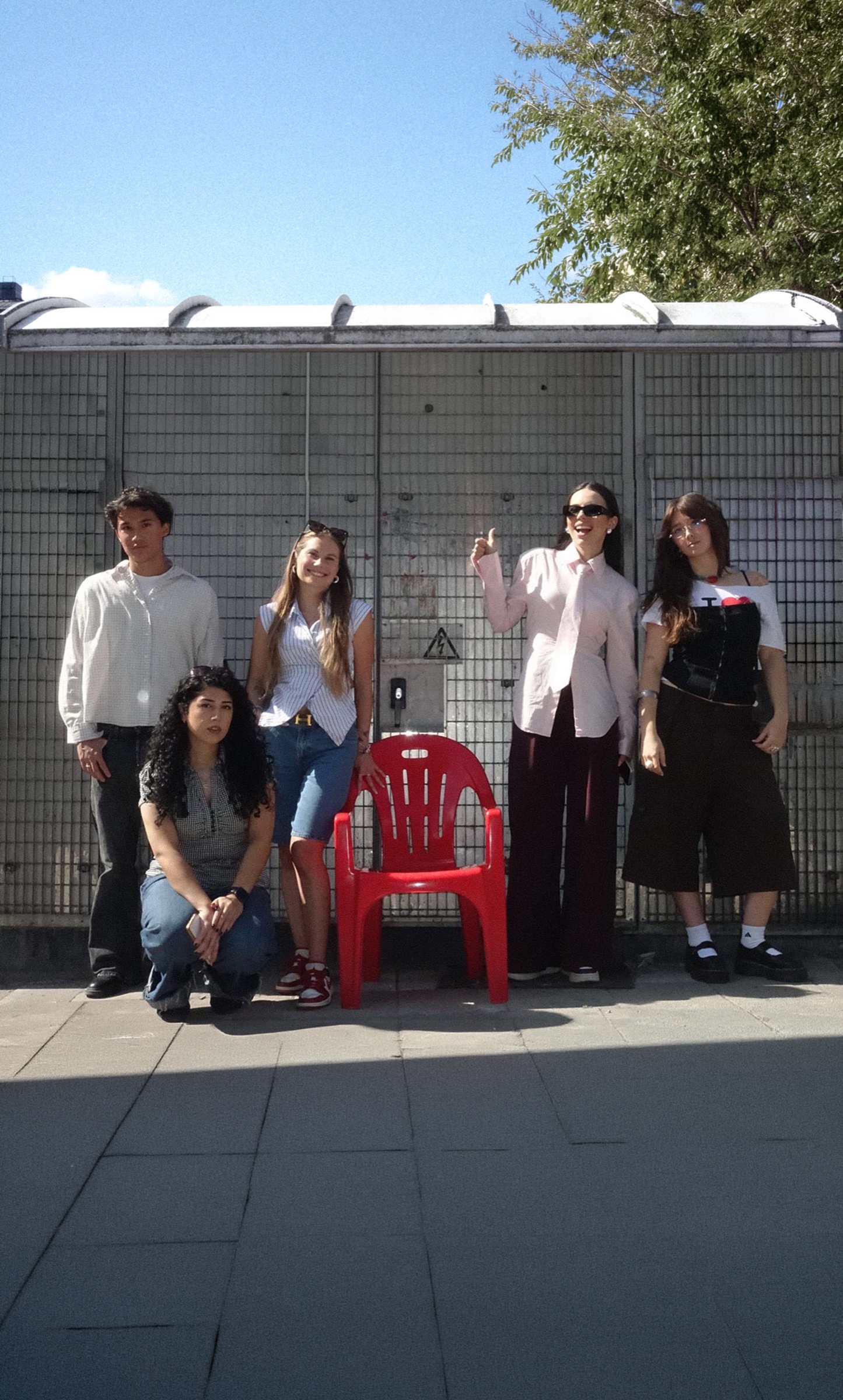 The Studio Neat team posing outdoors next to an empty red plastic chair